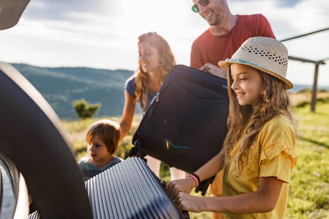 happy girl loading suitcases with her family into a car trunk before their trip for renault article