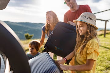 happy girl loading suitcases with her family into a car trunk before their trip for renault article