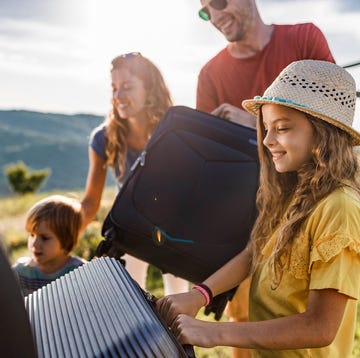 Happy family packing their luggage into a car trunk for Renault article happy girl loading suitcases with her family into a car trunk before their trip for renault article