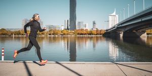 side view female mature adult athlete jogging alone along riverside in city on sunny day in autumn with urban skyline in background