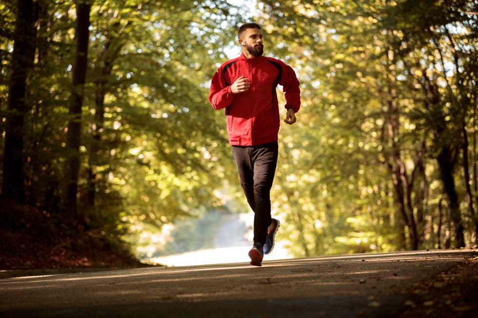 young athletic man with bluetooth headphones jogging in forest