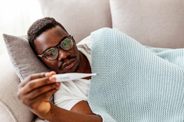 man ligt op bank en kijkt naar lichaamstemperatuur op thermometer