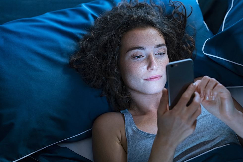 top view of young woman using a smartphone while lying on bed in the night high angle view of pretty girl messaging on smart phone before sleeping at night addicted woman suffering from insomnia and chatting and surfing on the internet with her cellphone late in night
