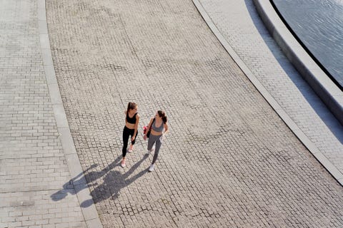 two women walking together along a paved path beside a body of water