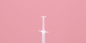 digital generated image of syringe stuck inside covid 19 vaccine bottle standing on blue surface against purple wall