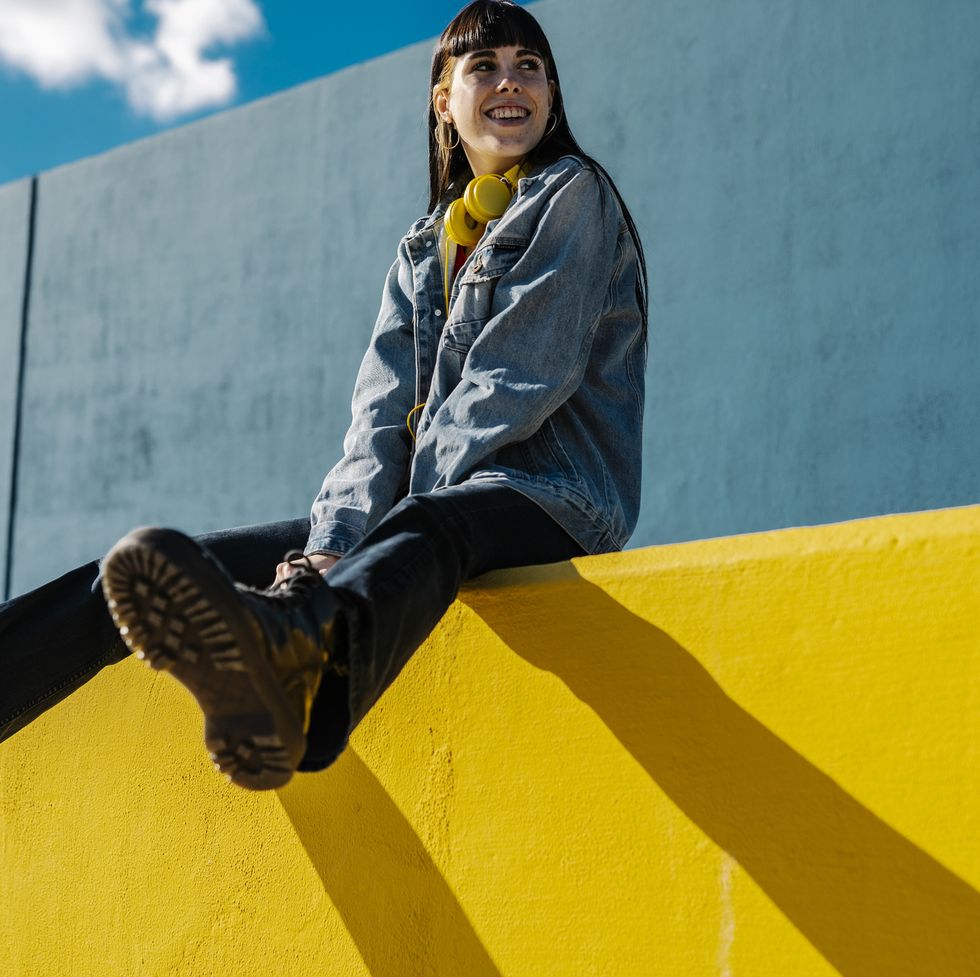smiling young woman sitting on a yellow wall in sunny day summer concept