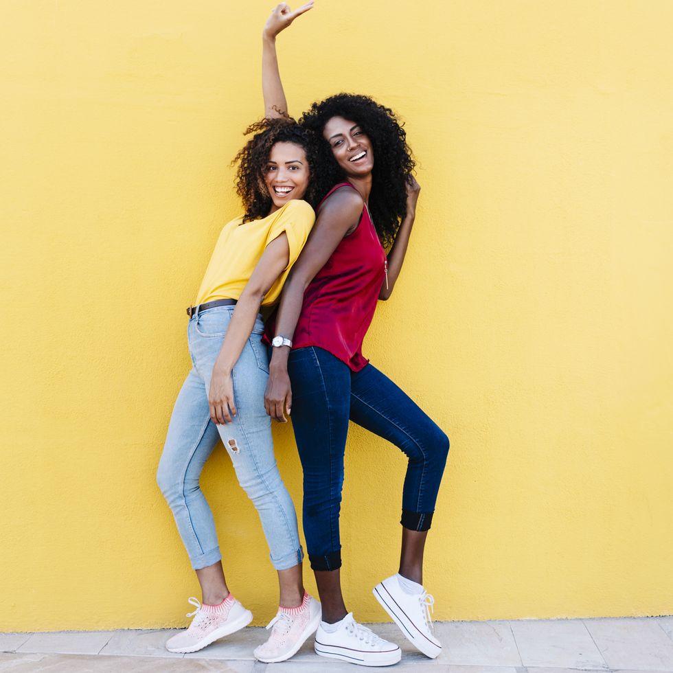 cheerful girlfriends enjoying while standing back to back by yellow wall