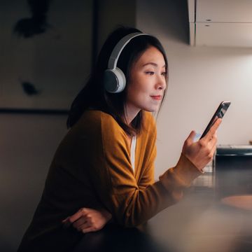 beautiful and smiling young asian woman listening to podcast on smartphone at home in the evening using smartphone for entertainment