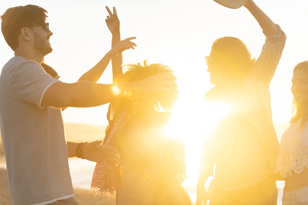 group of friends dancing and celebrating on the beach at sunrisesunset they are very happy, smiling and laughing some have their arms raised the sea and sun can be seen in the background defocussed with focus on background