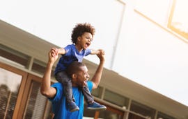 father carrying his little son on his shoulders while laughing and playing outside
