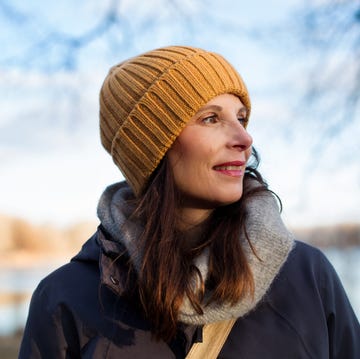A person wearing a beanie and scarf stands by a body of water A person wearing a beanie and scarf stands by a body of water