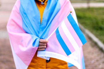 transgender woman covered with the transgender flag and holding a flag in the hand for defending her rights