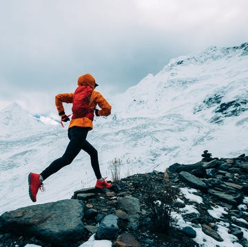 woman trail runner cross country running up to winter snow mountain top