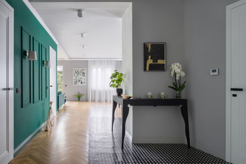 elegant and spacious apartment corridor with nice, green walls with molding and stylish black console table with decorations
