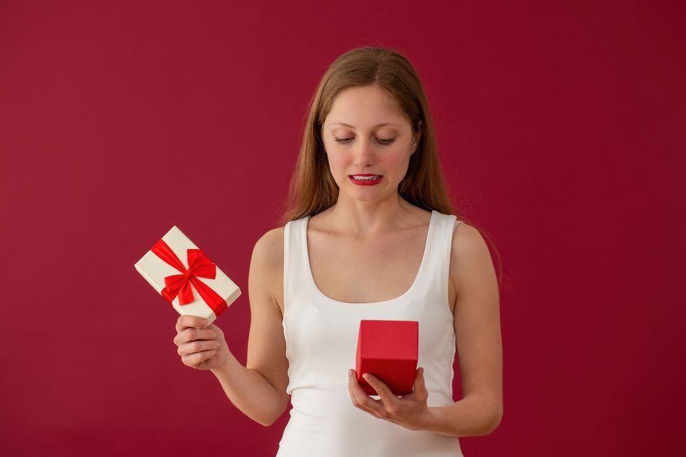 embarrassed woman looking on a present on red background dissappointed female with box in hands blonde girl confused by valentine gift