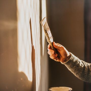 sunlight shines through a window, creating a sun beam on an interior wall a man holds a paintbrush and paints the wall a neutral colour simple and conceptual the shadow and wall provides a space for copy