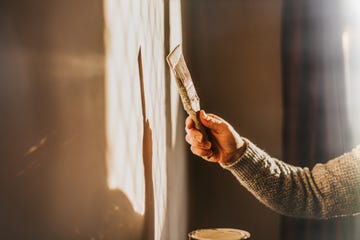 sunlight shines through a window, creating a sun beam on an interior wall a man holds a paintbrush and paints the wall a neutral colour simple and conceptual the shadow and wall provides a space for copy