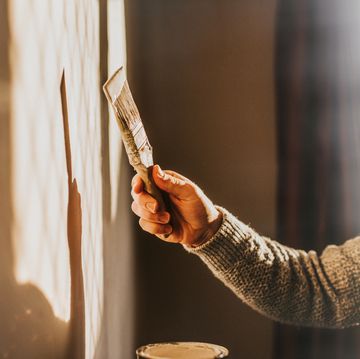 sunlight shines through a window, creating a sun beam on an interior wall a man holds a paintbrush and paints the wall a neutral colour simple and conceptual the shadow and wall provides a space for copy
