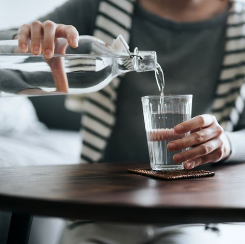 close up of young asian woman pouring water from bottle into the glass on a coffee table at home healthy lifestyle and stay hydrated
