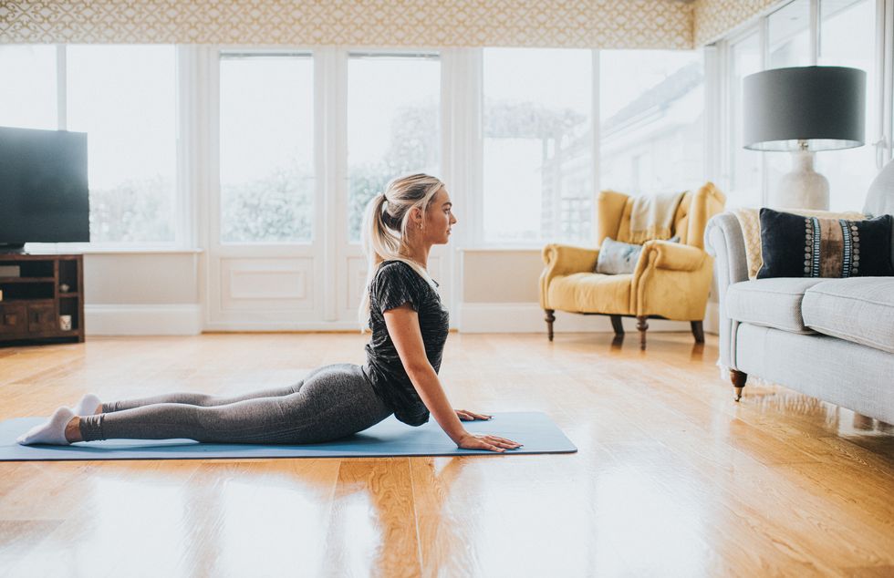 a young fit woman performs a cobra stretch on a yoga mat in a domestic room she does so with ease window provides space for copy