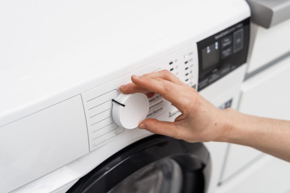 cropped view of woman choosing delicate cycle or select program at modern automatic washing machine. housewife regulate settings, turning knob on control panel. laundry and housework concept