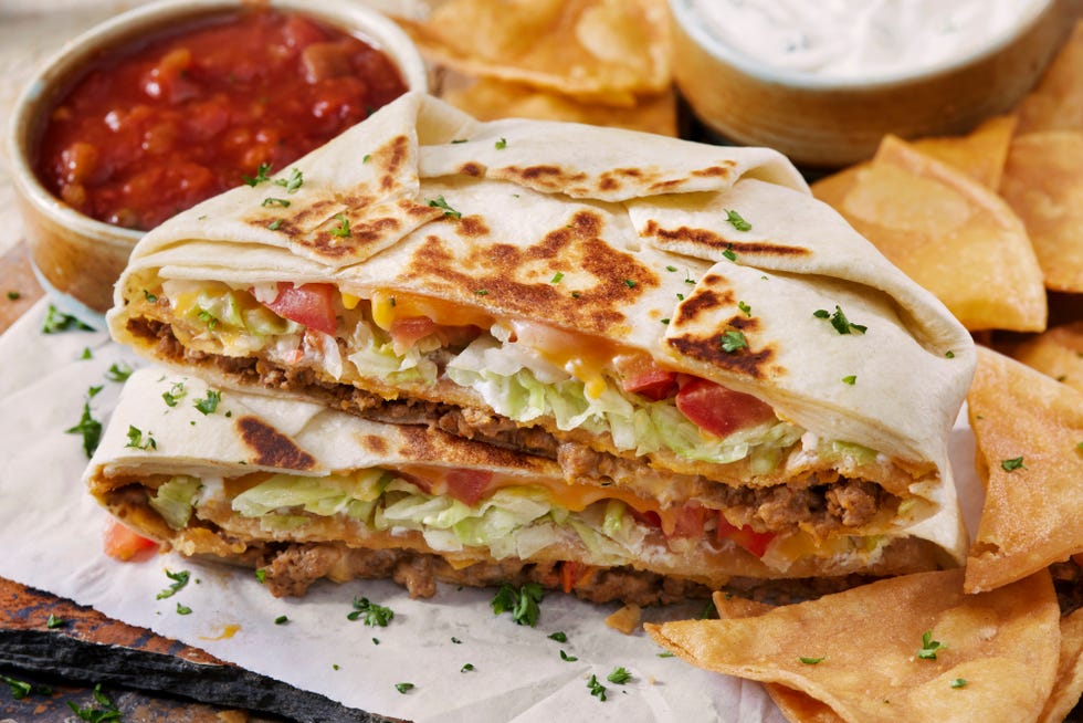 the copycat crunch wrap supreme with spicy ground beef, cheese, lettuce, tomato, sour cream, salsa con queso with a crispy corn tortilla in the middle
