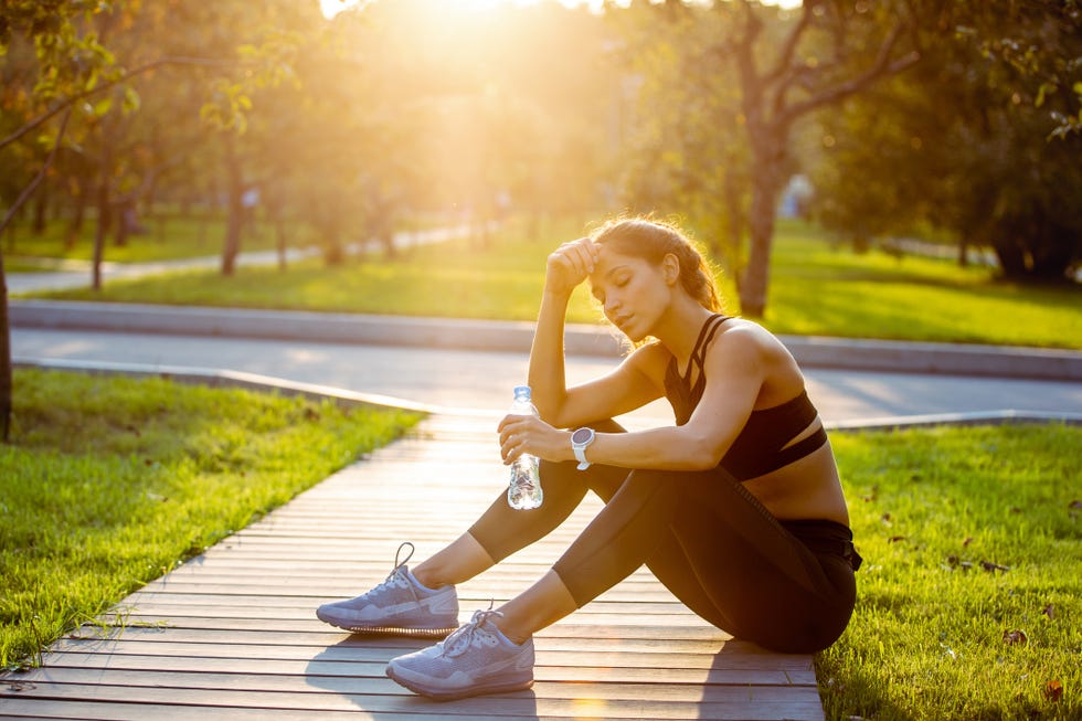 portrait of a sporty woman resting and hydrating with water after running outdoors and looking very tired