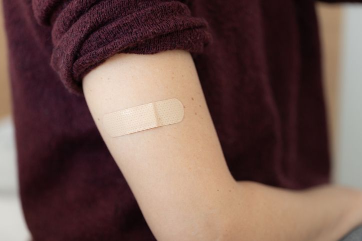 close up of a female patient young woman adhesive bandage to her own arm after taking vaccine