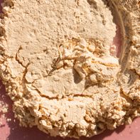 top view of close up spot of beige crushed face powder for makeup application on pink background copy space for your design