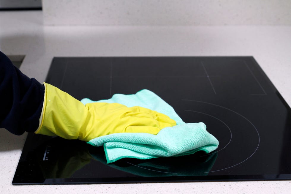 close up of hand with rubber glove cleaning induction stove with rag