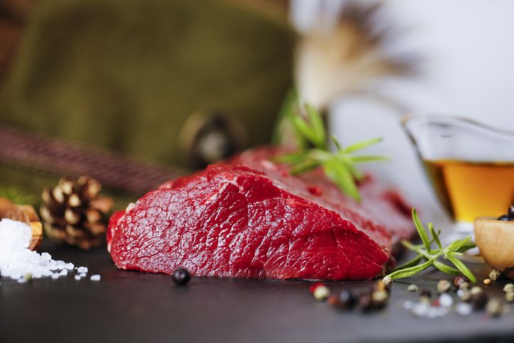 raw steak meat from deer on the bridlic  chopping board  with ingredients as a sea salt, pepper , rosemarine, oil and hunting hat as a decoration