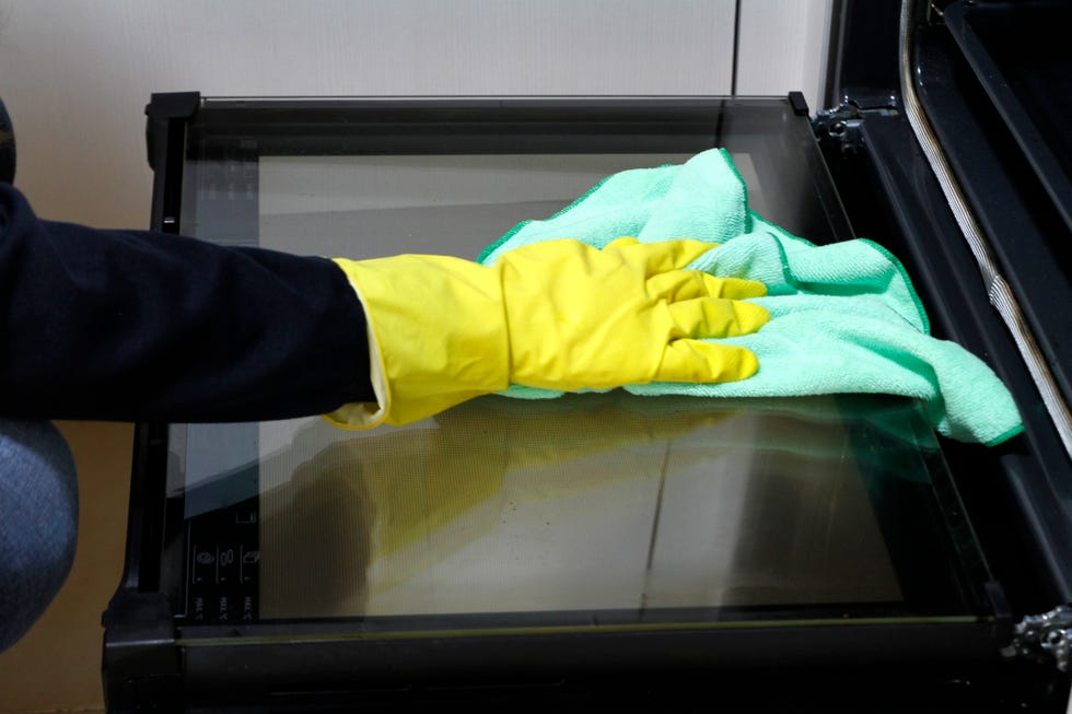close up of hand with rubber glove cleaning oven with rag