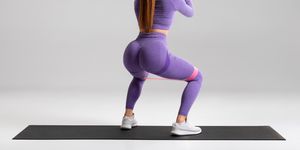 fitness woman doing squats exercise for glute with resistance band on gray background athletic girl working out