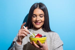 young woman eating muesli breakfast on blue backgroundstudio shot