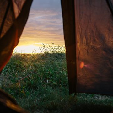 the open door of a tent overlooking the dramatic sunset and breidaik beach in icelands westfjords