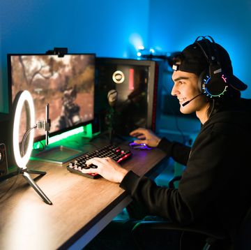 smiling young man live streaming his online video game using a smartphone and a ring light happy gamer ready to start playing in a gaming computer