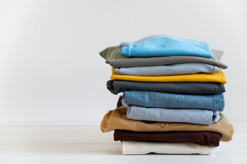 a stack of things on a white table or background, indoors. clean folded cotton denim clothing and bright colored t shirts. the concept of housework, ironing, care and storage of things. copy of the text space.