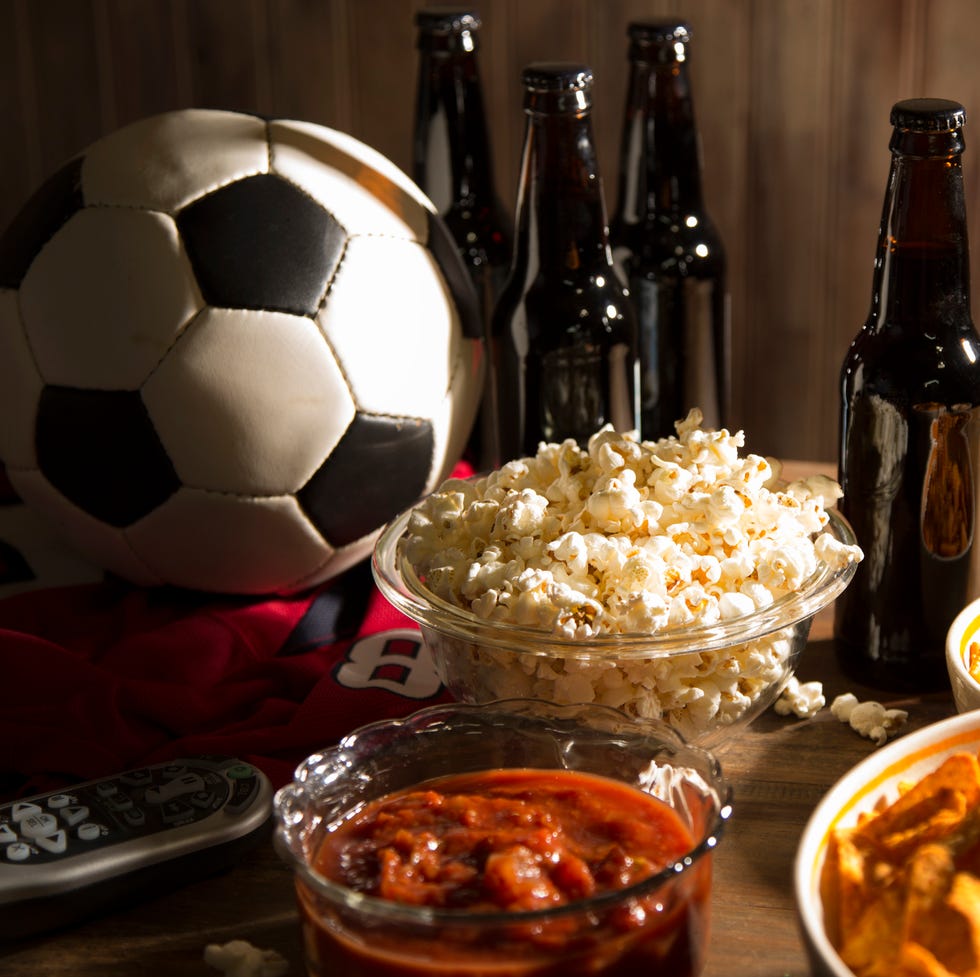 soccer season is here concept of sports fans watching the game on tv at home, at tailgate party, or sports bar with snacks and drinks tv remote, chips, football, soda, beer bottles
