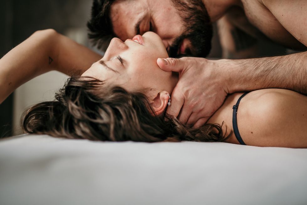 side view photo of a beautiful couple in bed, being gentle and sensual handsome guy with a beard on top of the beautiful brunette is kissing her neck while her eyes are closed making love concept