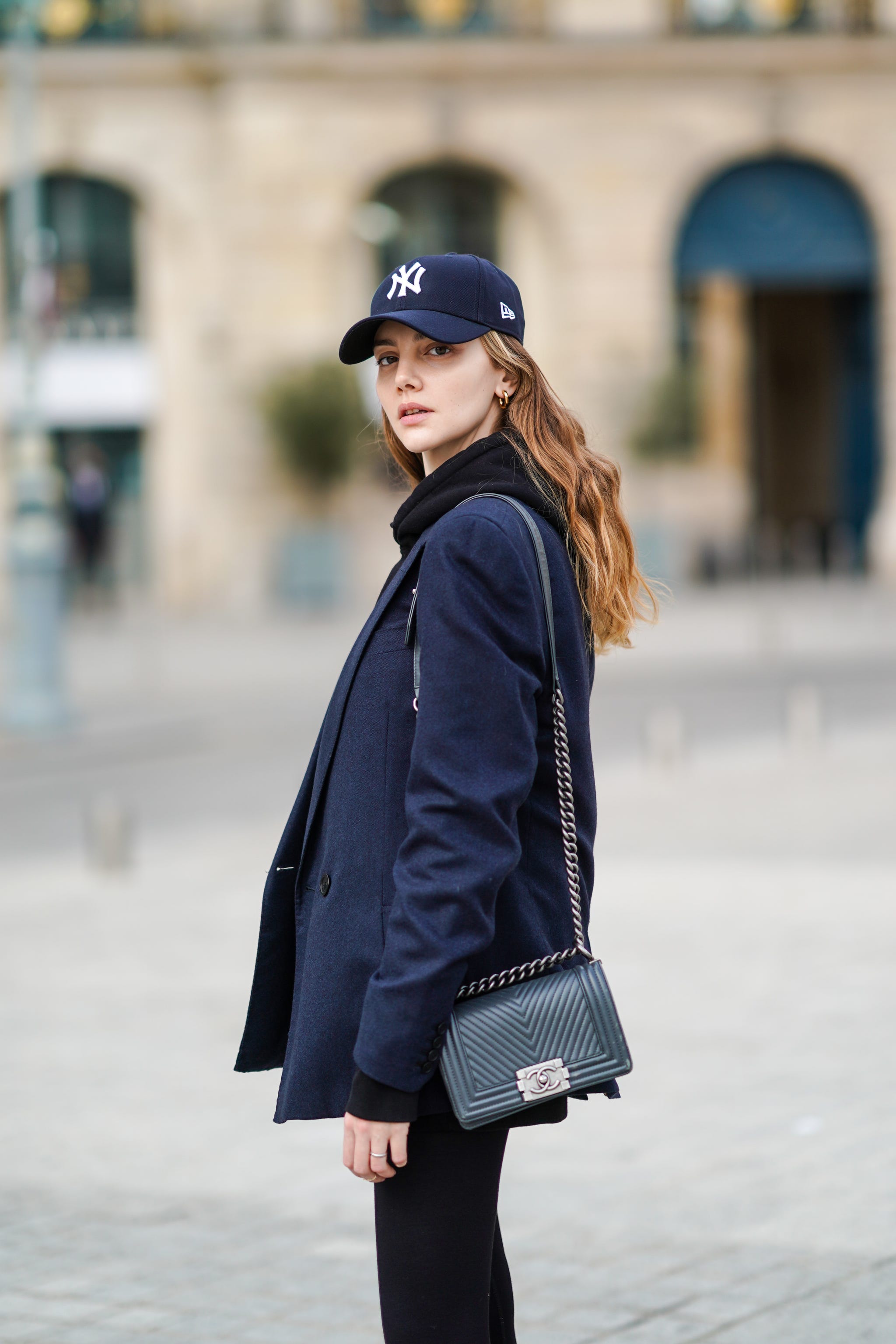 paris, france   march 03 olesya senchenko wears a ny blue cap hat, a black hoodie sweater, a navy blue blazer jacket, a black leather quilted chanel bag, black leggings, on march 03, 2021 in paris, france photo by edward berthelotgetty images
