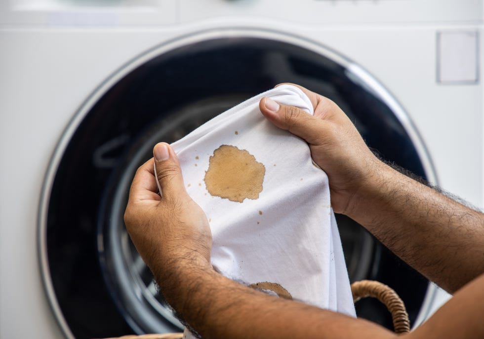 white cotton shirt a lot of stains, stains, coffee stains, mans hand holds the shirt up and spreads it to look dirty must be brought to the washing machine