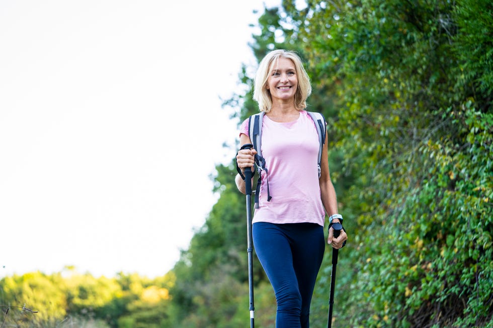 low angle view of smiling mature woman with hiking poles walking in forest