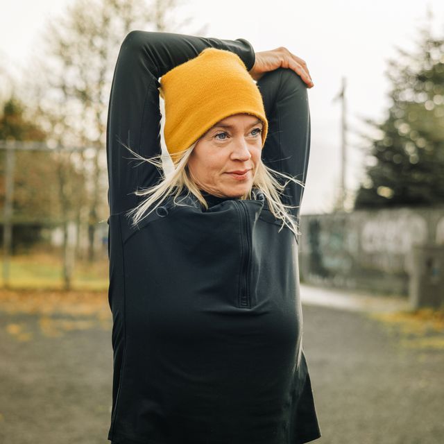 mature woman stretching arms in the city park female jogger wearing knitted hat doing warm up workout outdoor on a winter morning
