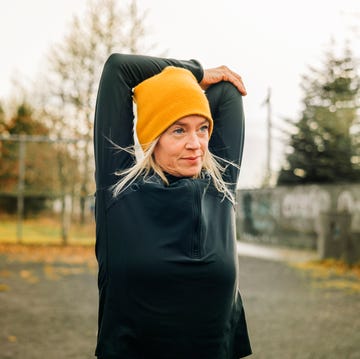 Jogger doing arm stretches in morning mature woman stretching arms in the city park female jogger wearing knitted hat doing warm up workout outdoor on a winter morning