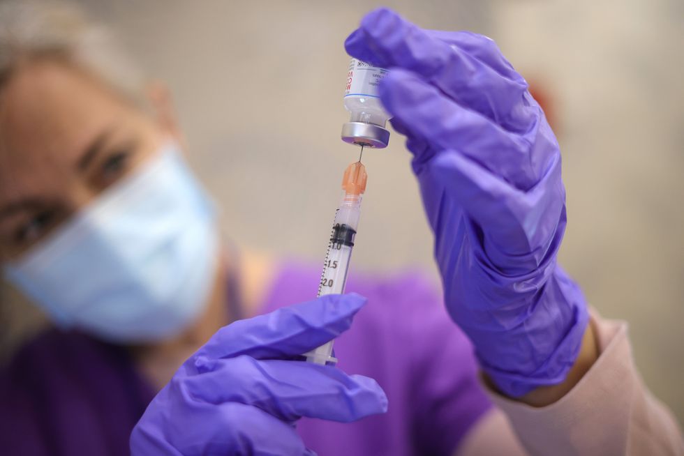 a woman doctor in purple scrubs fills a syringe