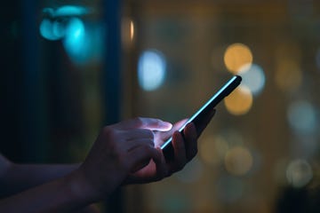 close up of womans hand using smartphone in the dark, against illuminated city light bokeh