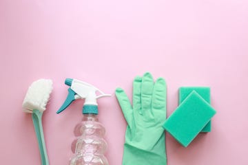 blue cleaning supplies bottle with chemicals, gloves, sponges and brushes over pink background flat lay with copy space