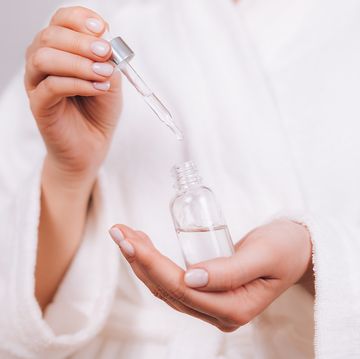 woman in white bathrobe with nude pink manicure holds pipette and transparent glass bottle with natural essential oil or organic serum she ready to start skin care procedures concept of home body care and healthy lifestyle close up front view