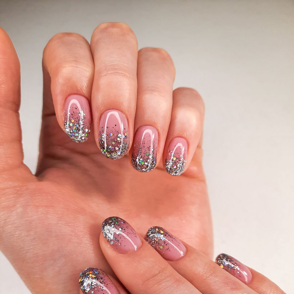 delicate camouflage coating with silver design hands in a sweater with pink gel polish and sequins stylish and shiny nail polish coating