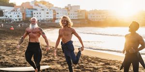 happy fit surfers with different age and race doing warm up exercises before surfing during sunset time extreme sport lifestyle and friendship concept